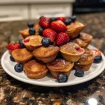 A close-up overhead shot of several mini pancake muffins with various toppings, including chocolate chips and fresh berries.