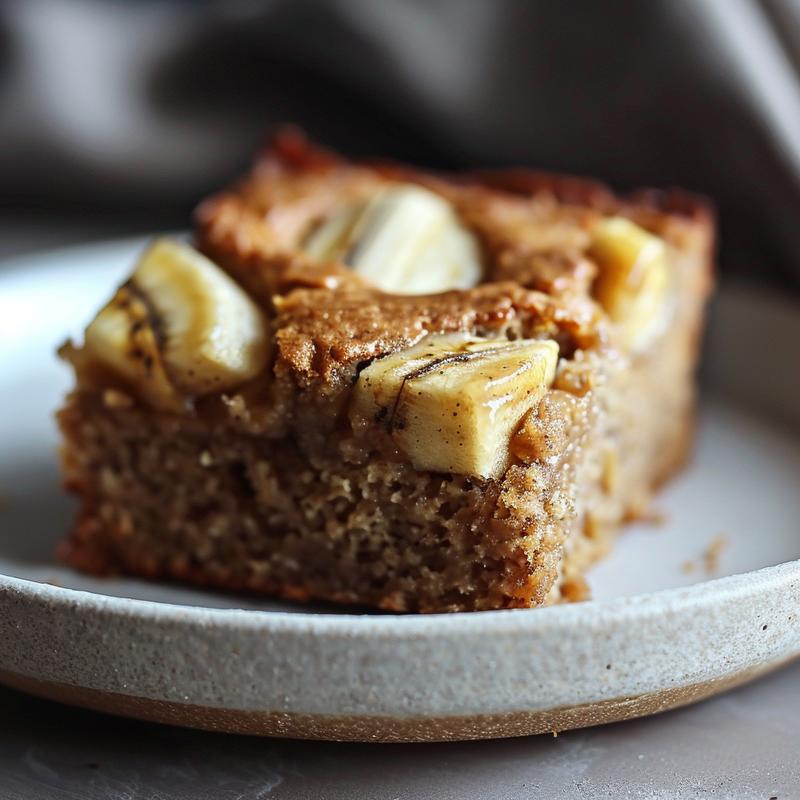 Close-up of a slice of low carb banana nut bread on a light grey plate, highlighting its moist texture and nutty appearance.